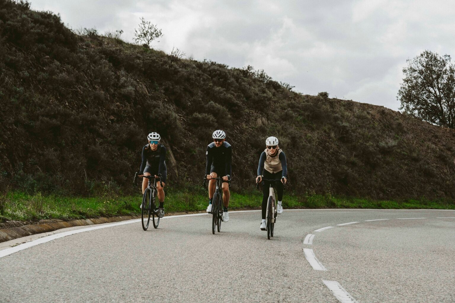 Grupo de ciclistas montando en bicicletas por la carretera en un tour de Castle Cycling. En una zona montañosa rodeada de naturaleza en Cataluña, todos llevan equipamiento especializado para tours de ciclismo en invierno